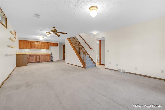 unfurnished living room with light colored carpet, visible vents, a textured ceiling, and stairs