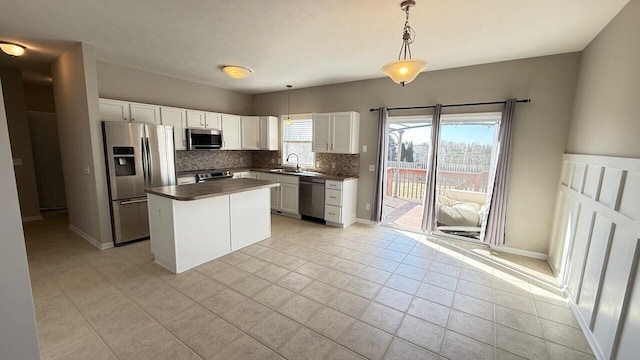 kitchen featuring tasteful backsplash, dark countertops, white cabinets, stainless steel appliances, and a sink