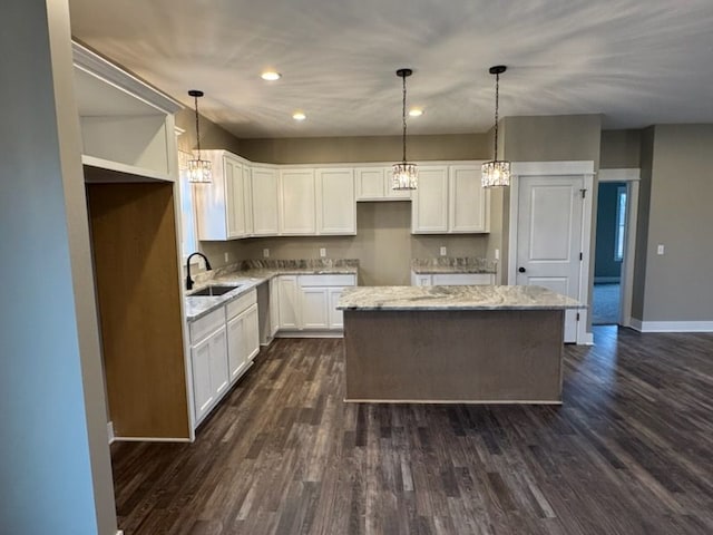 kitchen with dark wood-style floors, a kitchen island, light stone countertops, and a sink