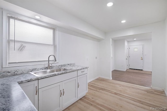 kitchen with light wood-style flooring, a sink, recessed lighting, white cabinets, and baseboards