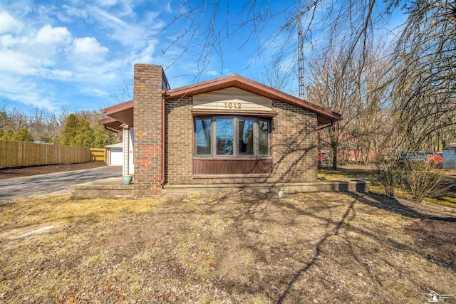 view of side of home with brick siding, driveway, a chimney, and fence