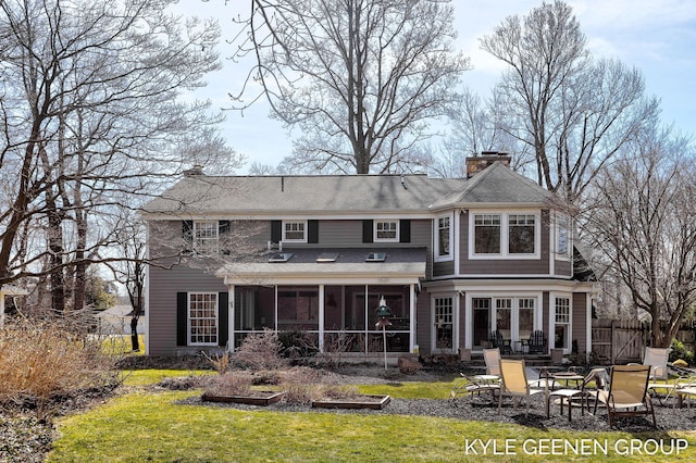 rear view of house with fence, a lawn, a chimney, a sunroom, and a patio