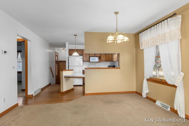 kitchen with visible vents, white appliances, a peninsula, and carpet floors