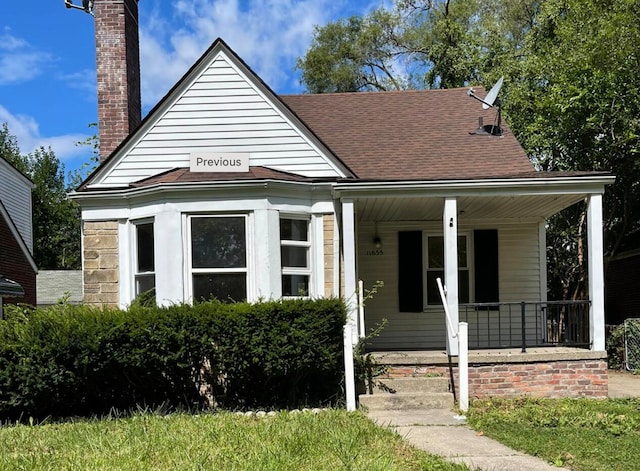 view of front facade with a chimney, covered porch, and a shingled roof