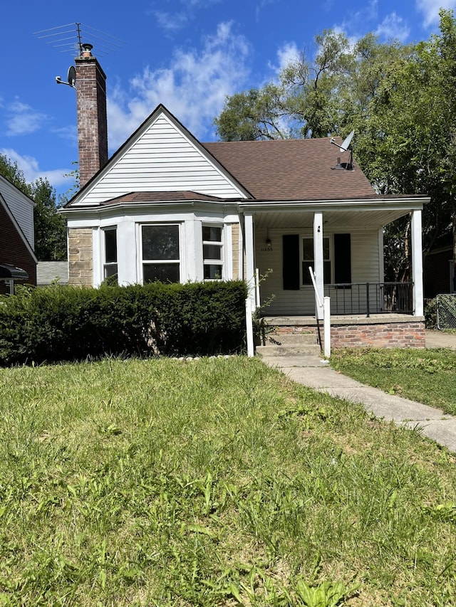 bungalow featuring covered porch, a chimney, a front lawn, and roof with shingles