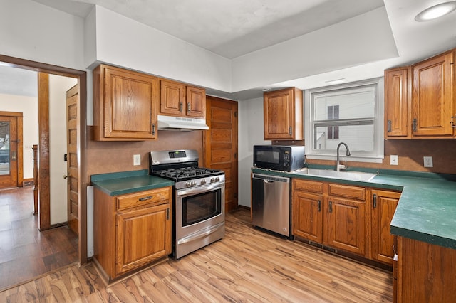 kitchen with under cabinet range hood, stainless steel appliances, brown cabinetry, and a sink