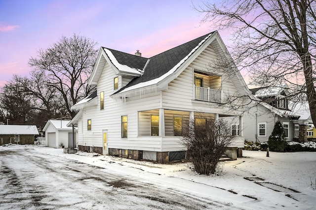 snow covered property with a garage, an outbuilding, a balcony, and a chimney