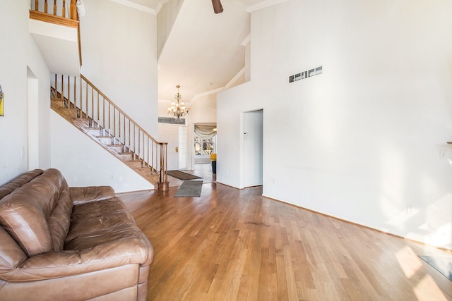 living room with stairway, wood finished floors, visible vents, an inviting chandelier, and a high ceiling