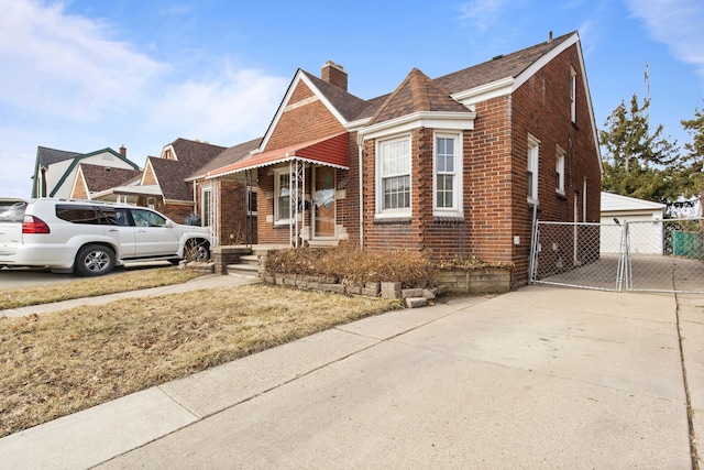 view of front of property with brick siding, a detached garage, fence, a chimney, and a gate