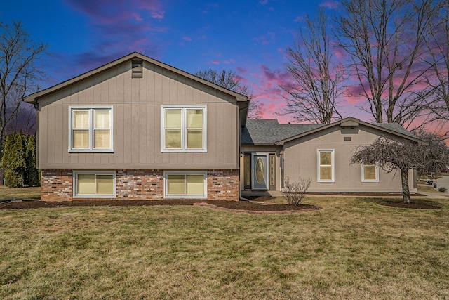 back of property with a yard, brick siding, and roof with shingles