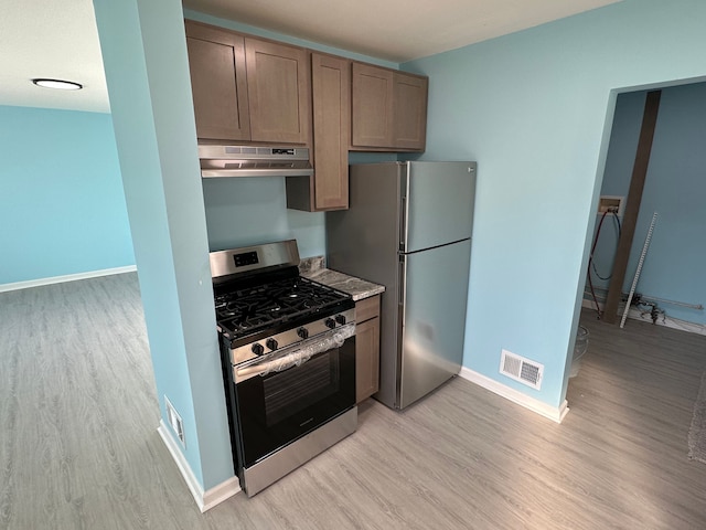 kitchen with light wood finished floors, visible vents, under cabinet range hood, stainless steel range with gas stovetop, and freestanding refrigerator