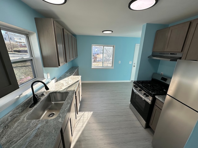 kitchen featuring plenty of natural light, stainless steel range with gas stovetop, freestanding refrigerator, a sink, and under cabinet range hood