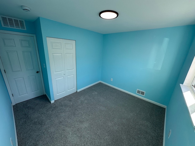 unfurnished bedroom with dark colored carpet, visible vents, baseboards, and a closet