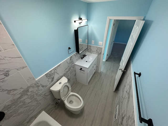 bathroom with a wainscoted wall, toilet, marble finish floor, tile walls, and vanity