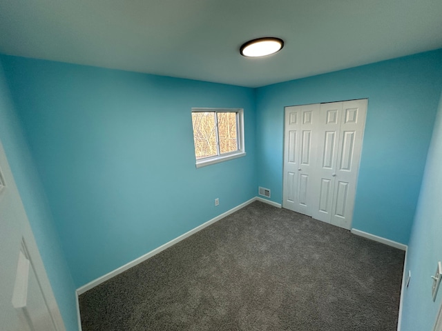 unfurnished bedroom featuring dark colored carpet, a closet, baseboards, and visible vents