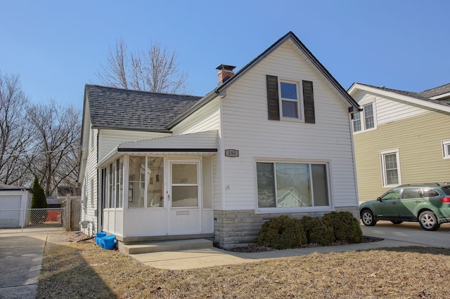 traditional home with fence, a sunroom, a chimney, a shingled roof, and stone siding