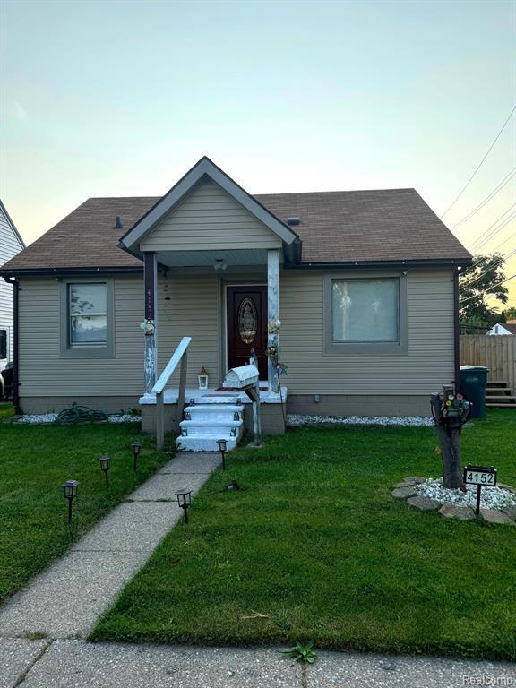 bungalow-style home with a front yard, fence, and roof with shingles