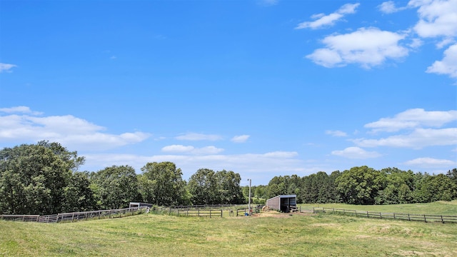 view of yard featuring a rural view, an outdoor structure, and fence