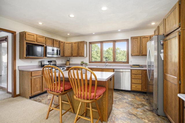 kitchen with a sink, stainless steel appliances, brown cabinetry, and light countertops