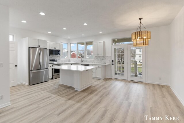 kitchen featuring light wood-style flooring, tasteful backsplash, stainless steel appliances, white cabinets, and light countertops