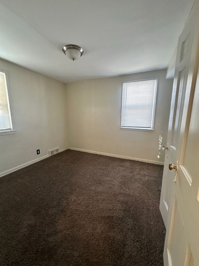 empty room featuring baseboards, visible vents, and dark carpet