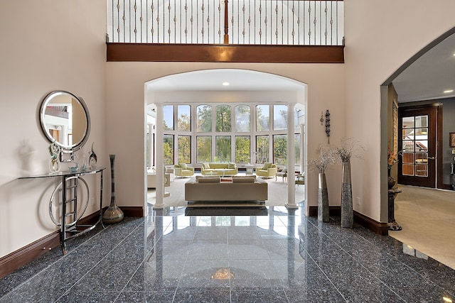 entryway featuring baseboards, a high ceiling, arched walkways, and granite finish floor