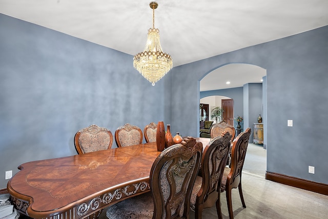 dining area featuring baseboards, arched walkways, light carpet, and a chandelier