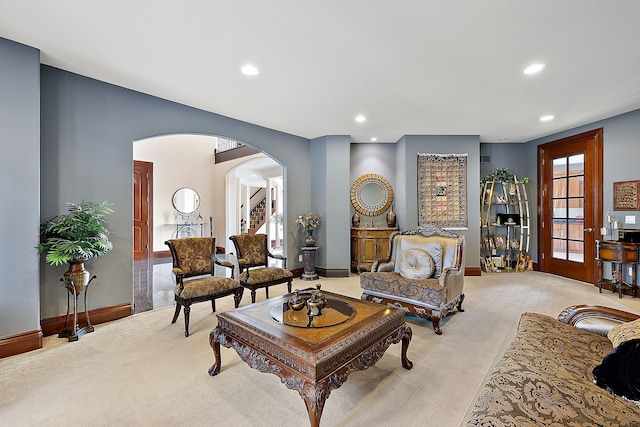 living area featuring baseboards, recessed lighting, arched walkways, stairs, and light colored carpet