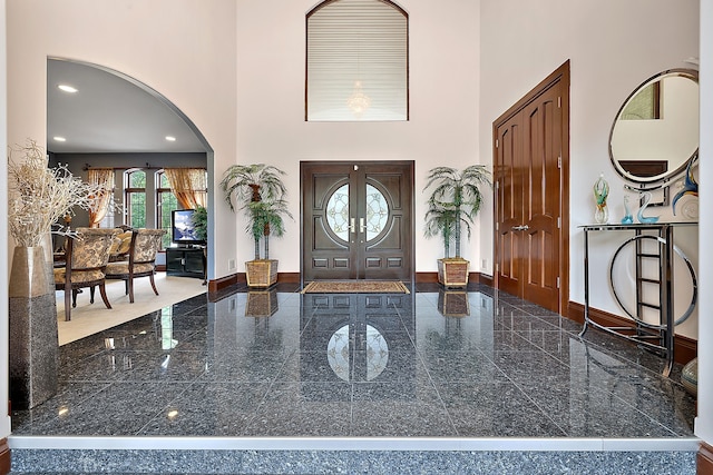 entrance foyer with granite finish floor, recessed lighting, arched walkways, a high ceiling, and baseboards