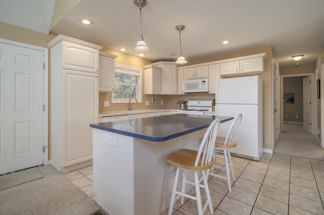 kitchen with white appliances, light tile patterned floors, a breakfast bar, a sink, and white cabinetry