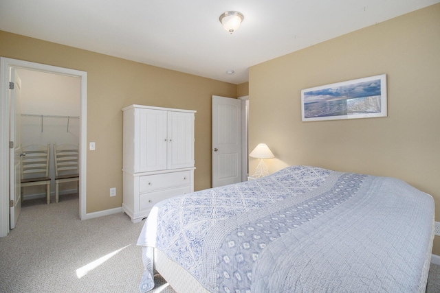 bedroom with a walk in closet, baseboards, a closet, and light carpet