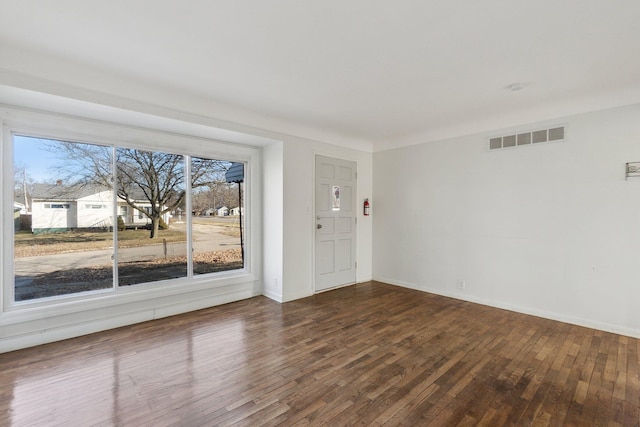 empty room featuring visible vents, dark wood-type flooring, and baseboards