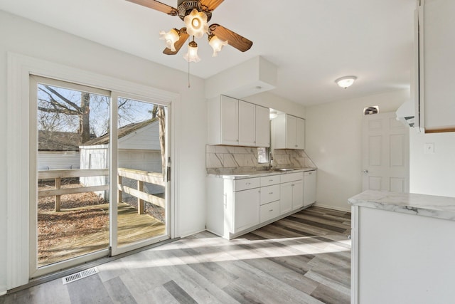 kitchen with visible vents, a sink, white cabinetry, light wood finished floors, and decorative backsplash