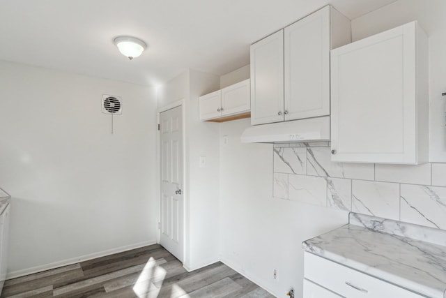 kitchen featuring under cabinet range hood, tasteful backsplash, white cabinetry, light wood finished floors, and baseboards