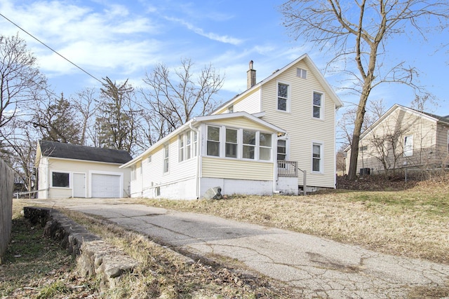 view of front of home featuring a chimney, a garage, a sunroom, an outbuilding, and driveway