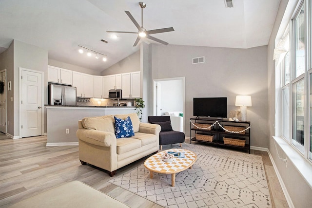 living room with visible vents, baseboards, light wood-style floors, and high vaulted ceiling