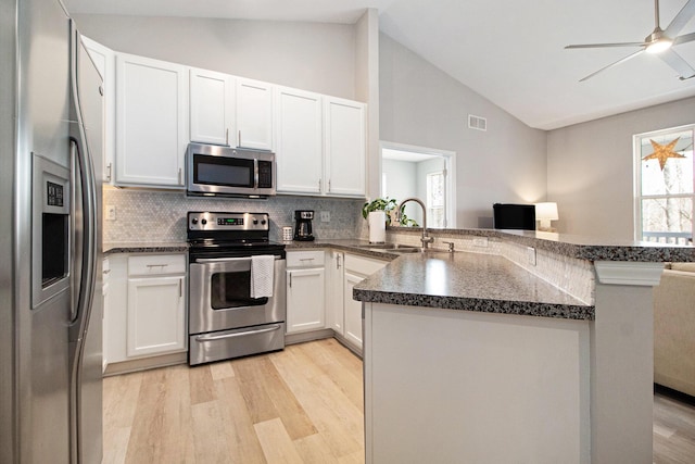 kitchen with lofted ceiling, a peninsula, a sink, light wood-style floors, and appliances with stainless steel finishes