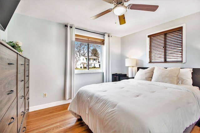 bedroom with light wood-style flooring, a ceiling fan, and baseboards