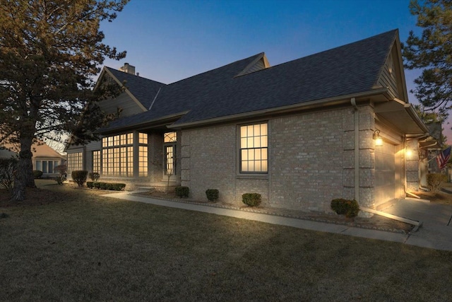 view of side of home with brick siding, a shingled roof, a chimney, a yard, and an attached garage