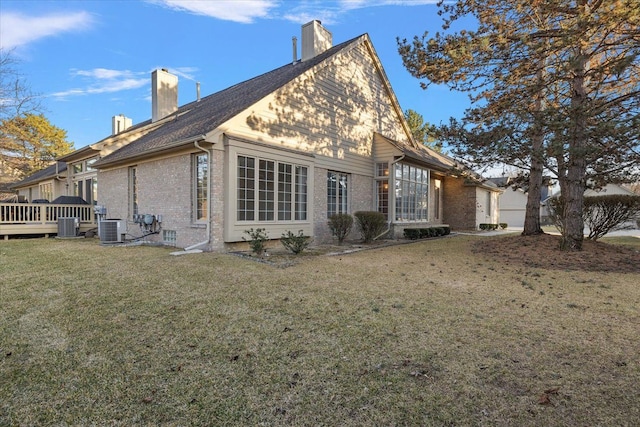 back of property with brick siding, central AC unit, a chimney, and a lawn