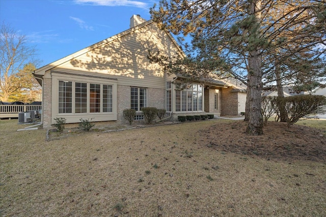 back of house with brick siding, a lawn, central AC, and a chimney