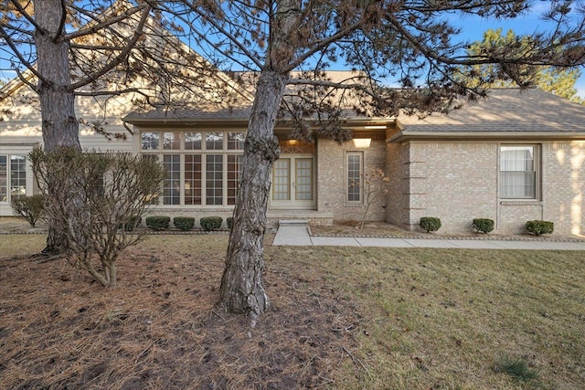 rear view of house with a yard, french doors, brick siding, and a shingled roof