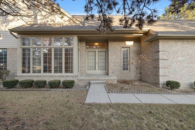 doorway to property featuring a lawn, french doors, brick siding, and a shingled roof