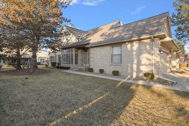 view of side of home featuring a lawn, an attached garage, a shingled roof, brick siding, and a chimney