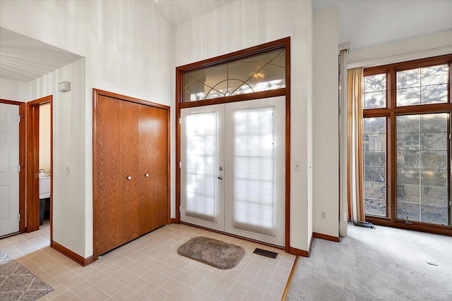 entryway with visible vents, baseboards, light colored carpet, french doors, and a towering ceiling