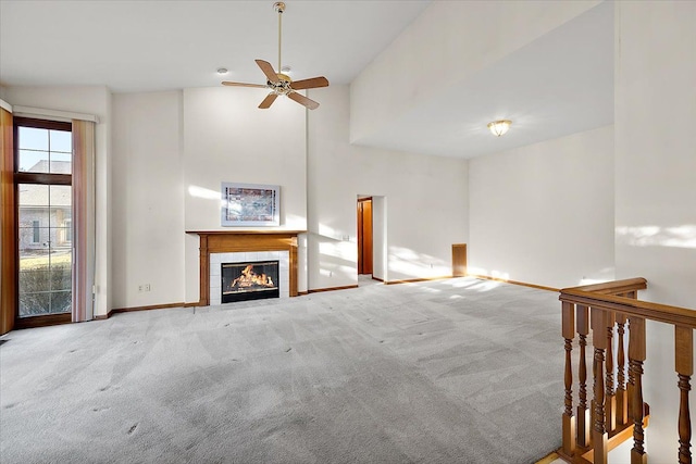 unfurnished living room with a ceiling fan, baseboards, carpet floors, a towering ceiling, and a tiled fireplace