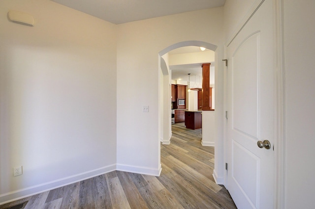 hallway with visible vents, wood finished floors, baseboards, and arched walkways