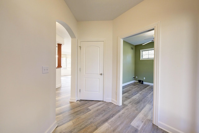 corridor featuring wood finished floors, arched walkways, and baseboards