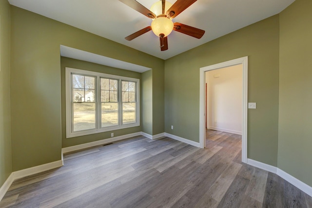 spare room featuring a ceiling fan, visible vents, wood finished floors, and baseboards