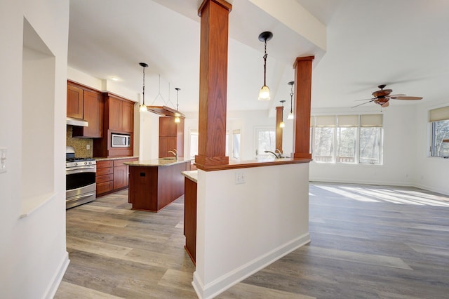 kitchen with under cabinet range hood, open floor plan, decorative backsplash, light wood-style floors, and stainless steel appliances